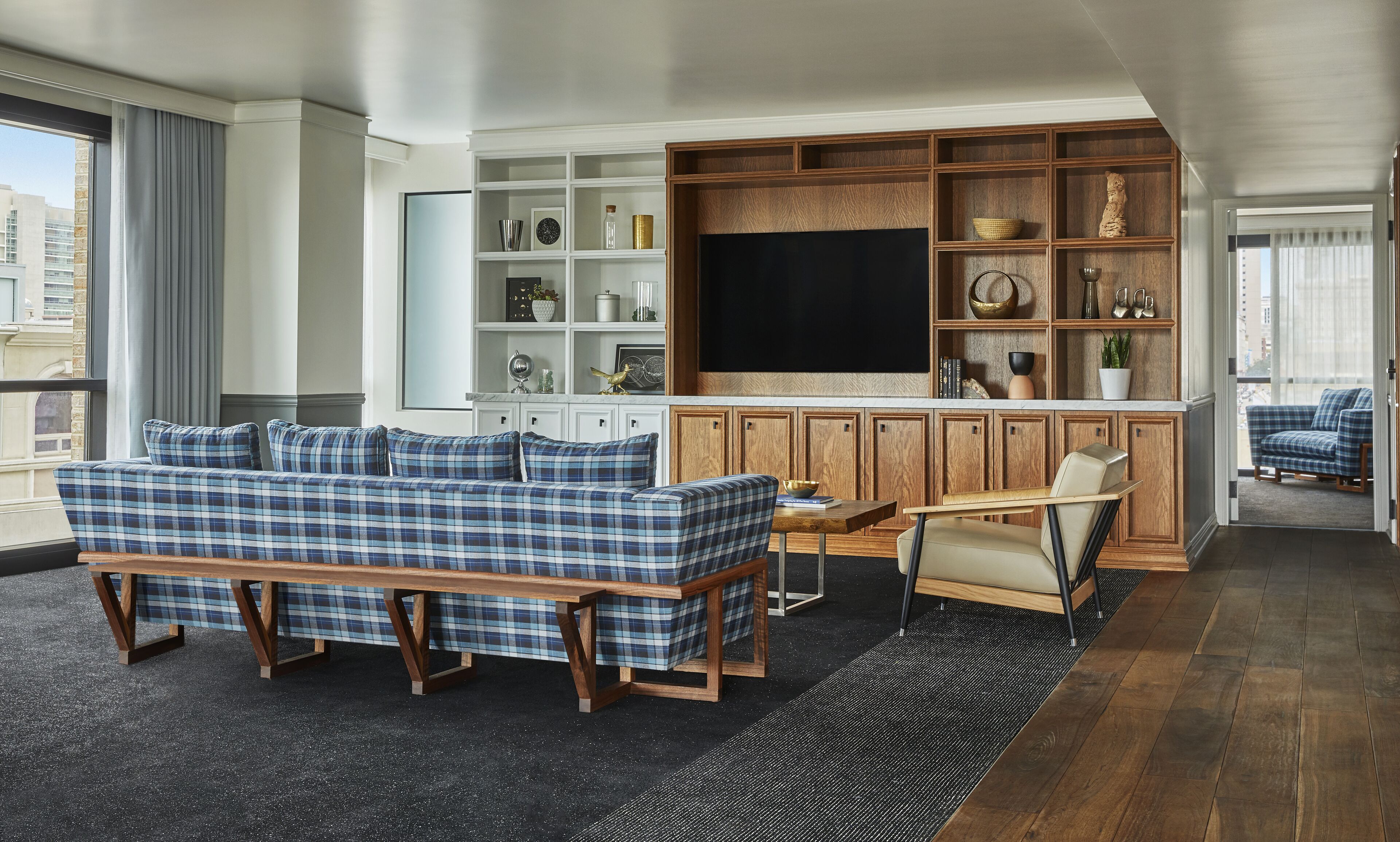 A living room with a blue plaid sofa, a wooden coffee table, and a TV mounted on a wooden cabinet.