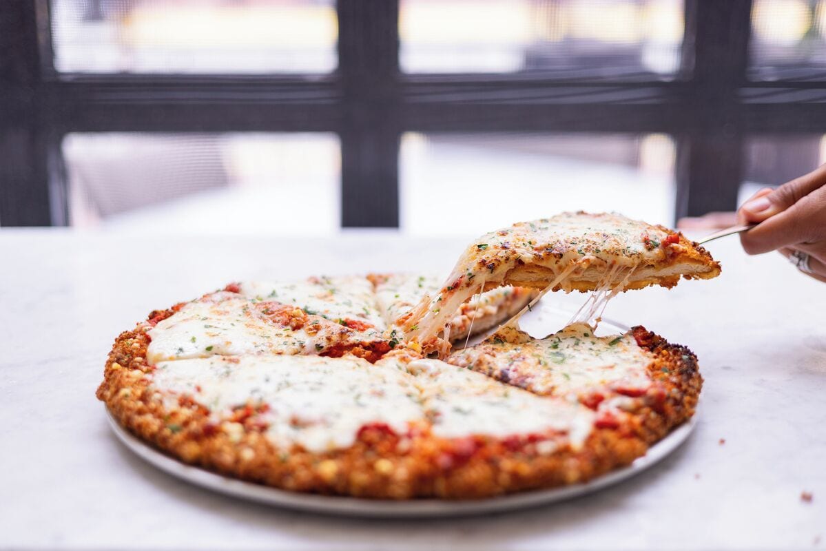 Una pizza con una porción levantada, sobre un plato blanco.