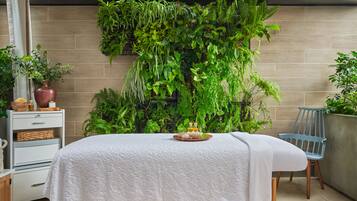 A spa area with a massage table, a chair, and a wall of greenery.