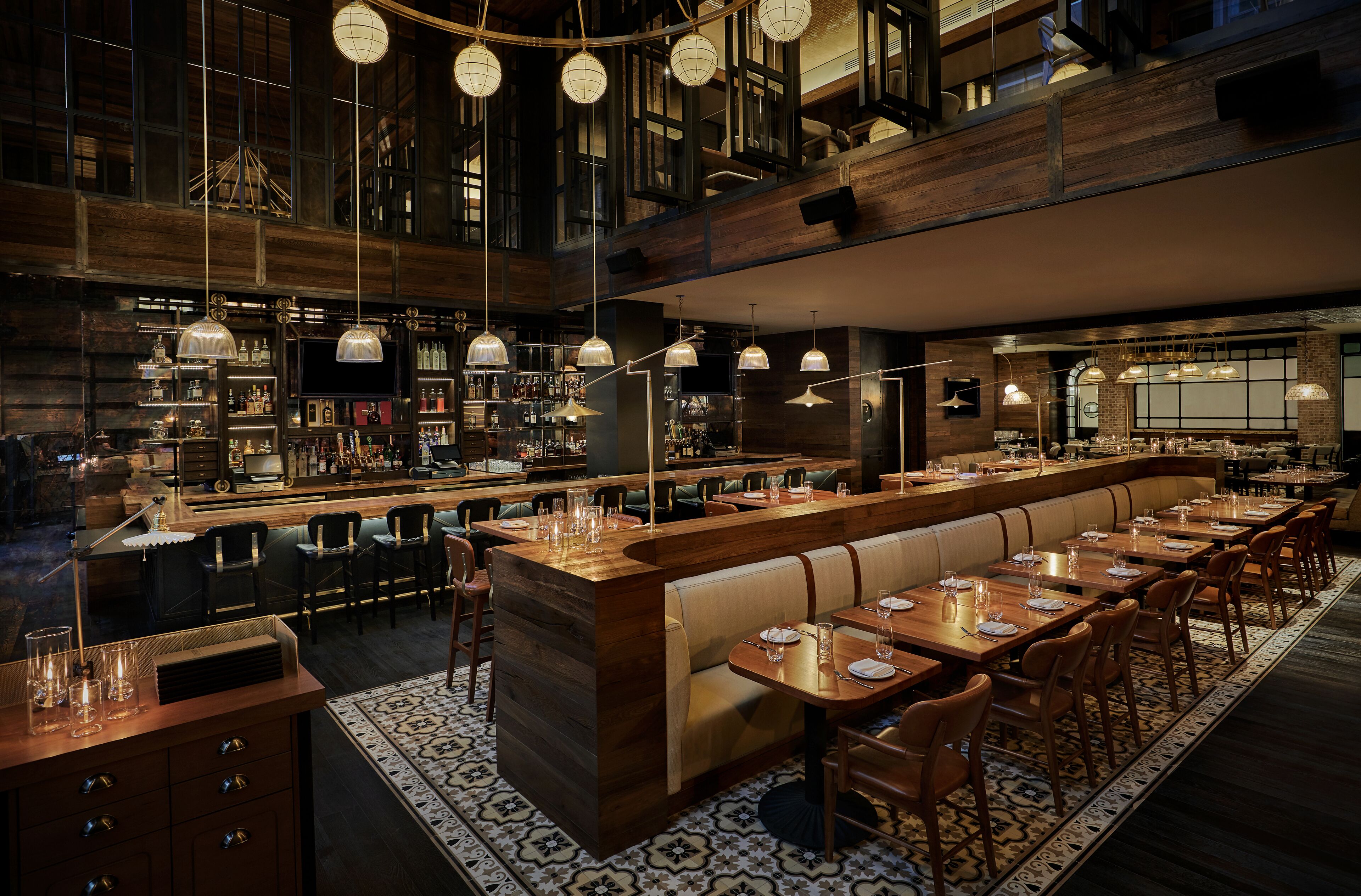 Un espace bar moderne avec des comptoirs en bois, des luminaires suspendus et un coin salon avec des tables et des chaises.
