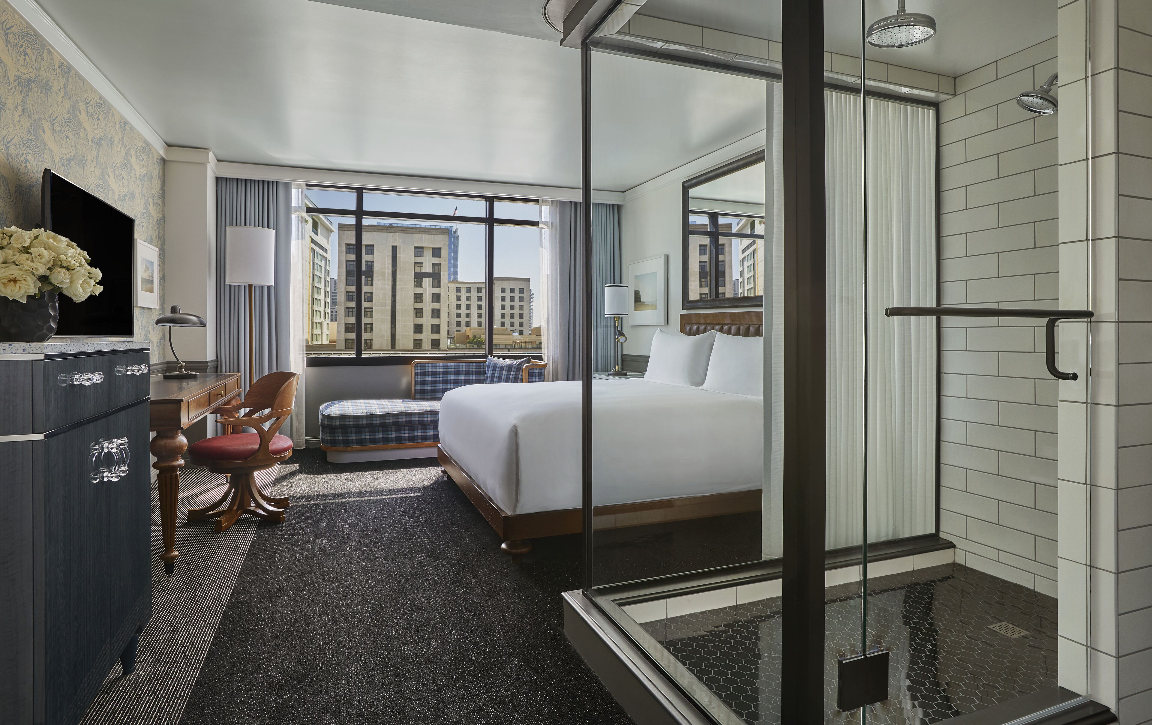 Habitación de hotel con cama, escritorio, silla, ducha y vista a la ciudad.