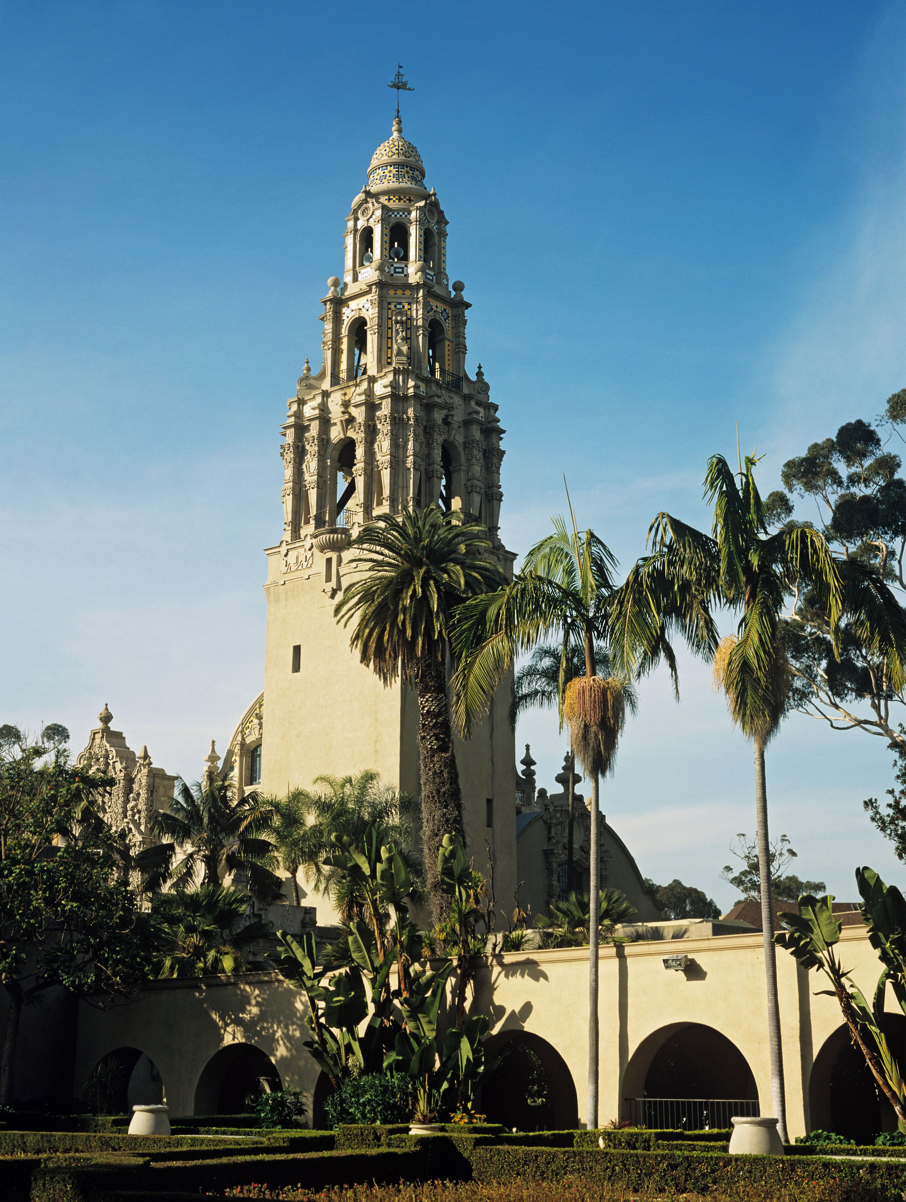 Un edificio histórico con un campanario, rodeado de palmeras y un jardín bien cuidado.