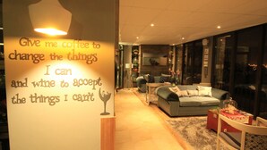 A cozy living room with a large window, a sofa, a coffee table, and a wall with motivational text. - Bay View Guest House Somerset West (Cape Town)