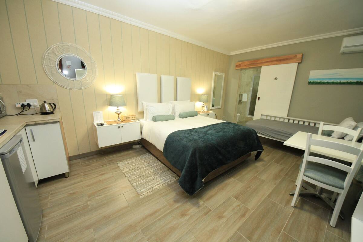 A hotel room with a bed, bedside tables, a desk, a chair, a mirror, and a wardrobe.