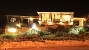 A modern two-story house with a well-lit facade, large windows, and a landscaped garden in front. - Bay View Guest House Somerset West (Cape Town)