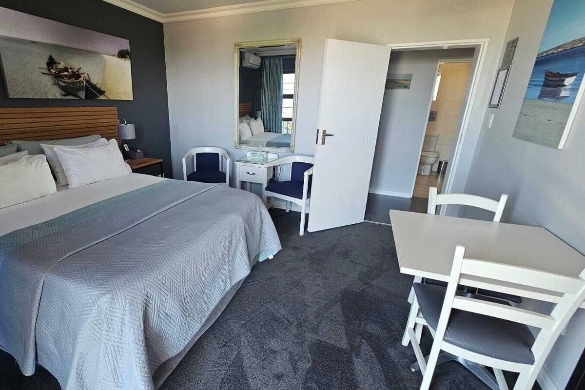 A hotel room with a bed, a desk, a chair, and a mirror.
