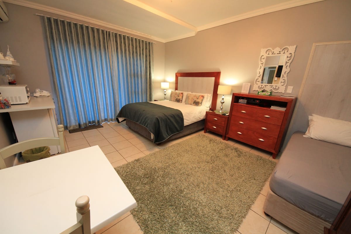 A hotel room with a bed, a wooden dresser, a desk, and a chair.