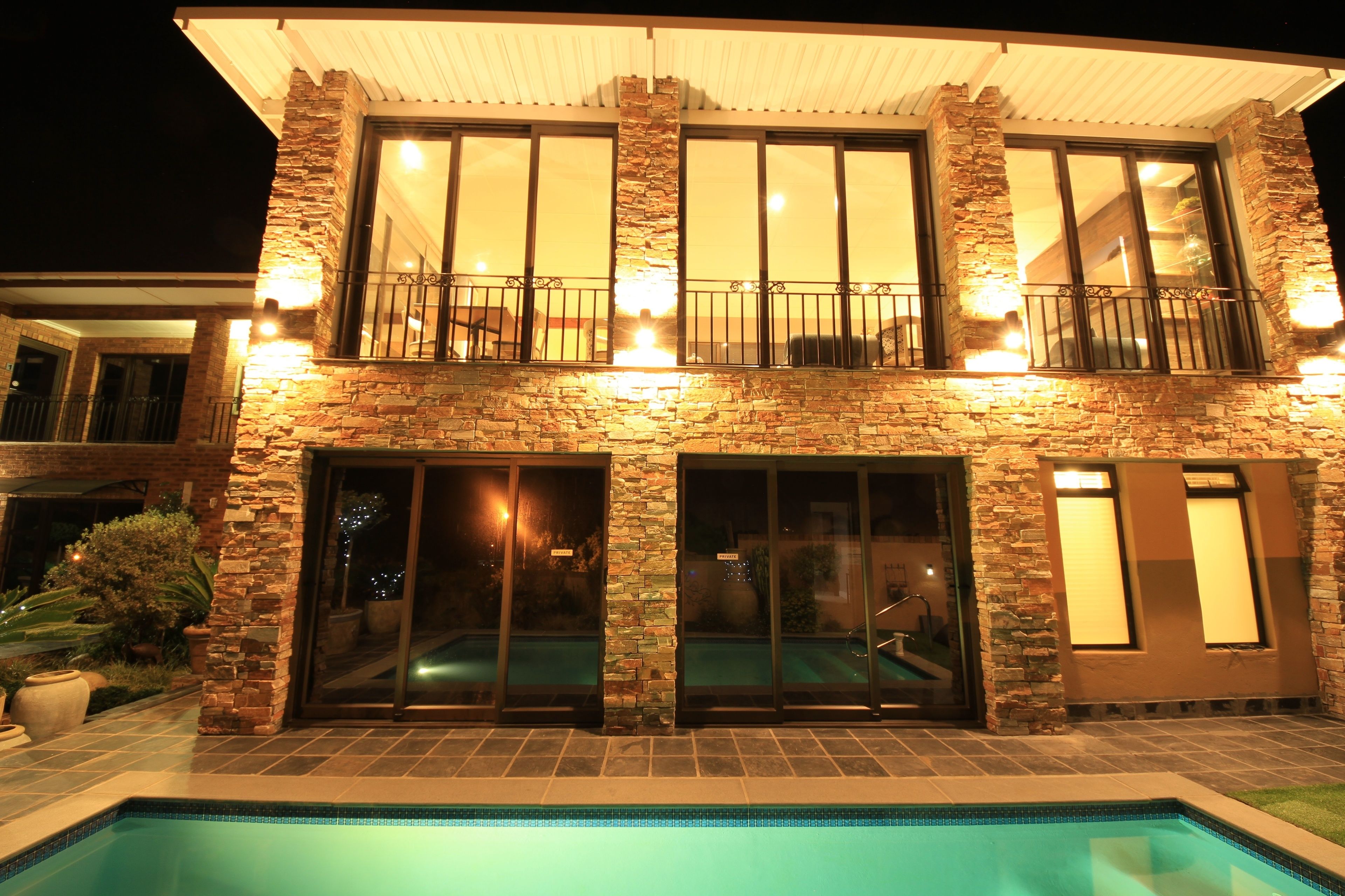 Une maison à deux étages avec une piscine, une façade en pierre et de grandes fenêtres.