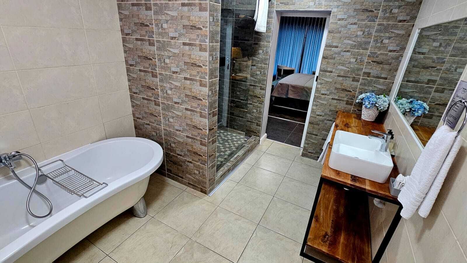 Un baño con una bañera independiente, un tocador de madera con lavamanos y una zona de ducha con puerta de cristal.