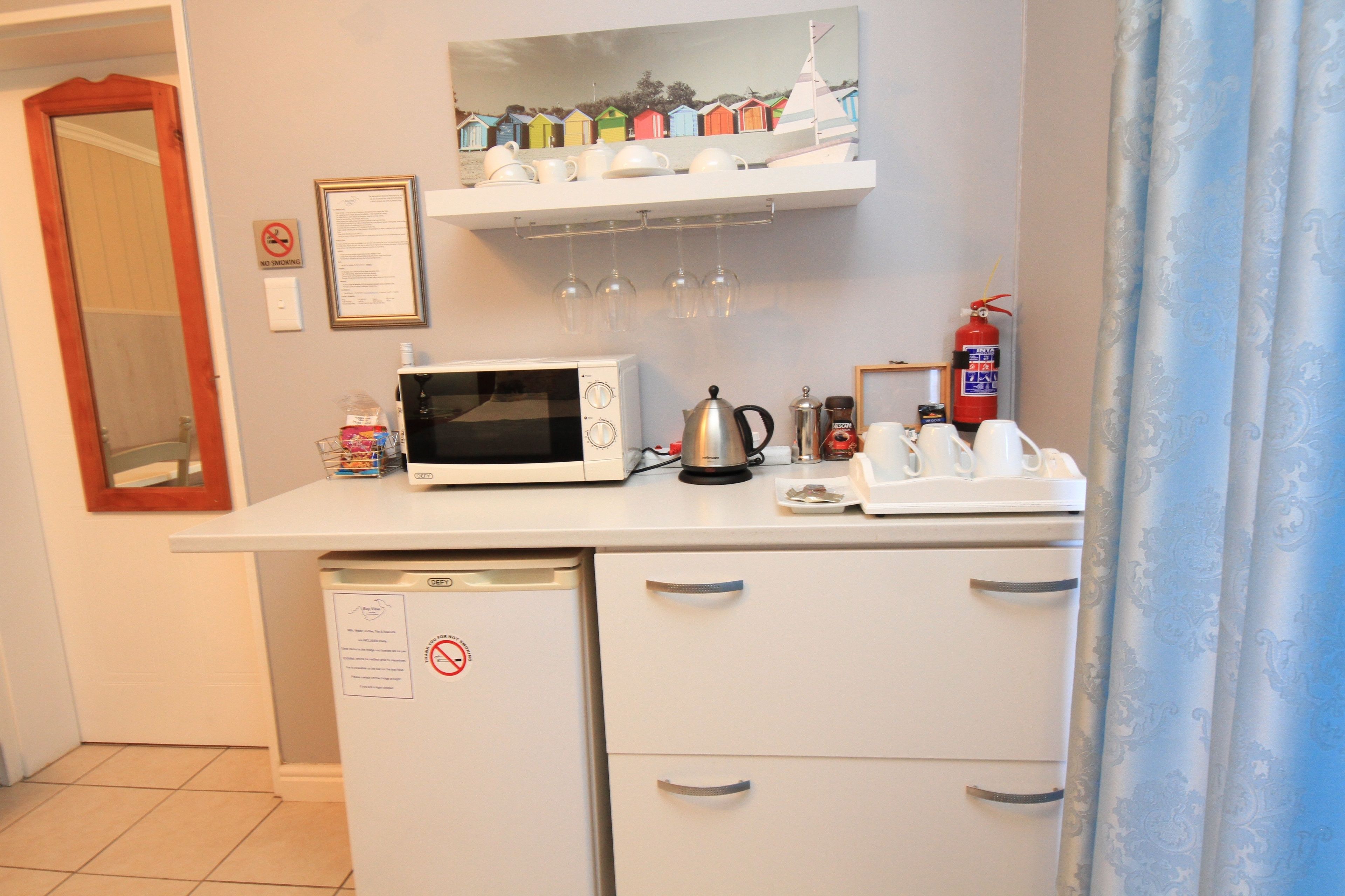 A kitchenette with a microwave, coffee maker, and a small shelf with cups and glasses.