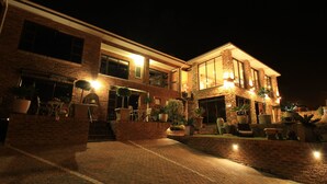 A two-story building with a brick facade, large windows, and outdoor seating areas with potted plants. - Bay View Guest House Somerset West (Cape Town)