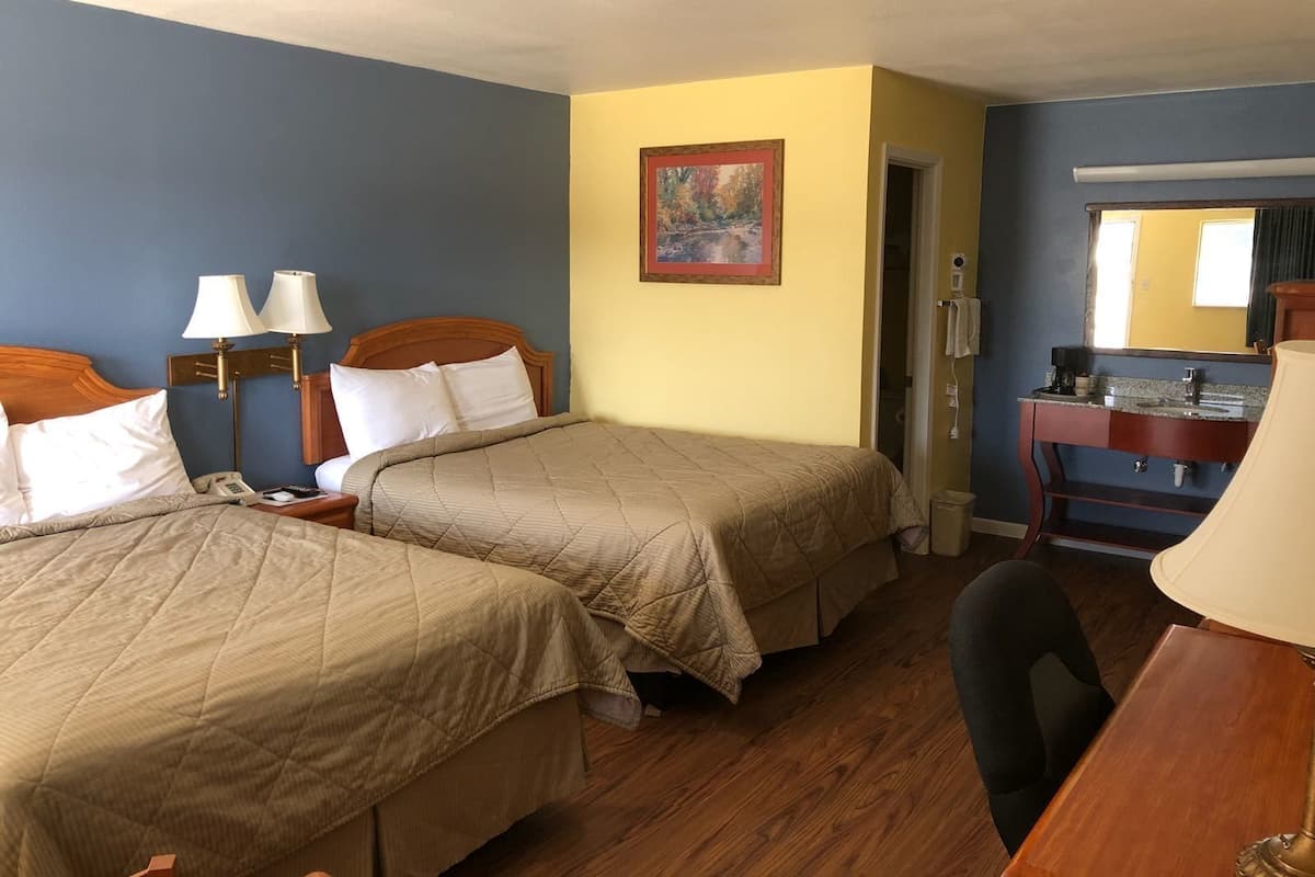 A hotel room with two beds, a desk, a chair, a mirror, and a painting on the wall.