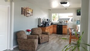 A modern kitchen with a stone backsplash, wooden cabinets, and a built-in island with a sink. There are two upholstered chairs and a potted plant in the living area. - Gold Key Inn (Brady)