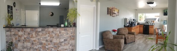 A modern kitchen with a stone backsplash, wooden cabinets, and a built-in island with a sink. There are two upholstered chairs and a potted plant in the living area.