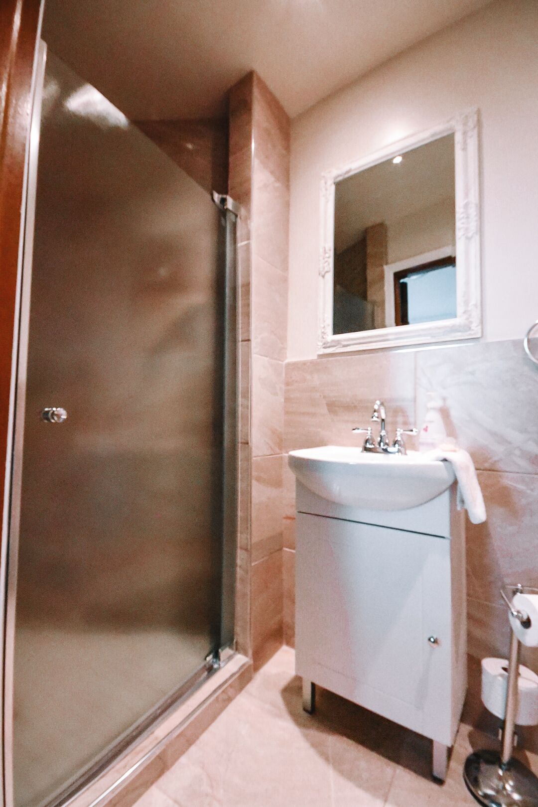 Un baño con mampara de vidrio, un lavamanos blanco y un espejo encima.