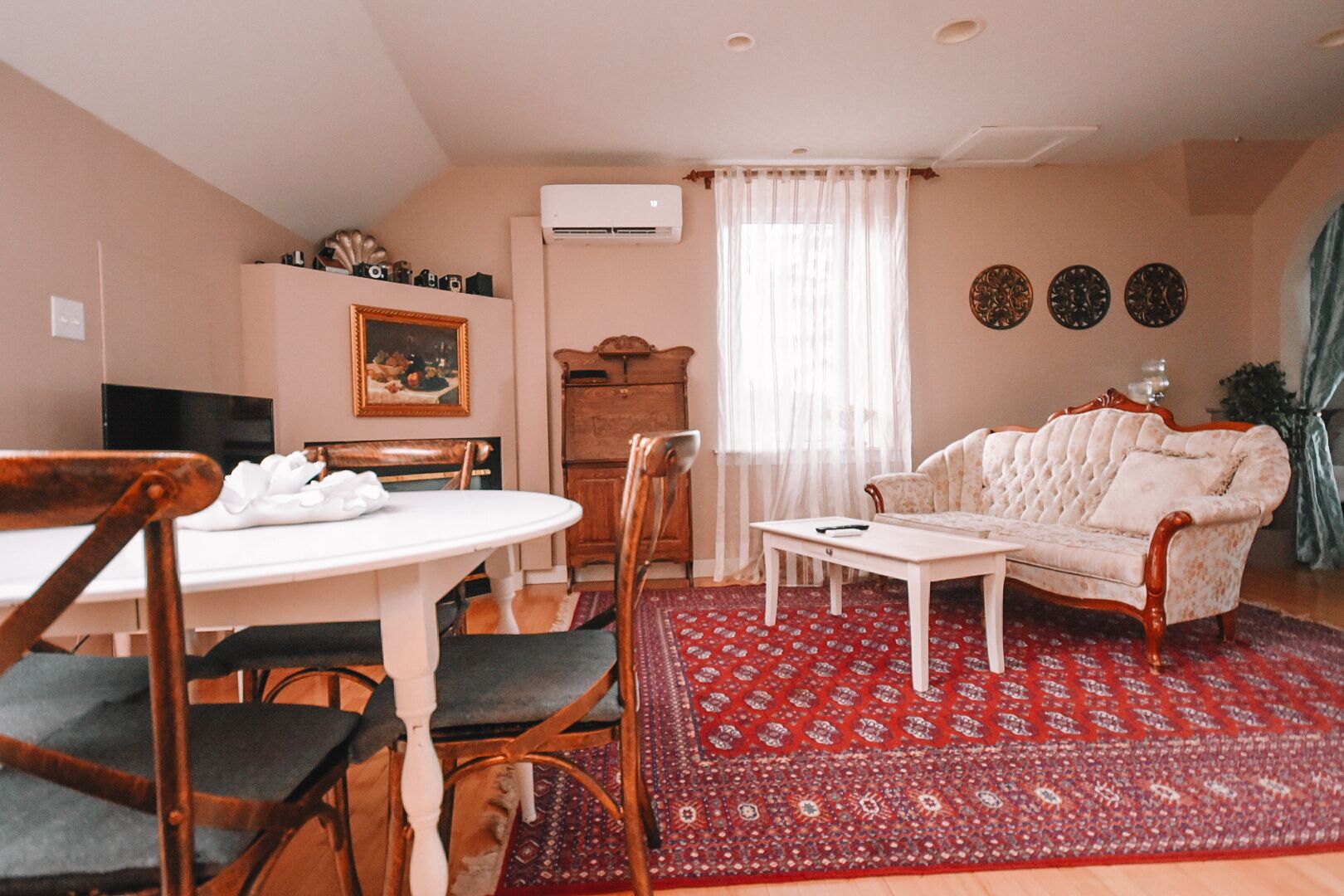 A living room with a dining table, chairs, a sofa, and a patterned rug.