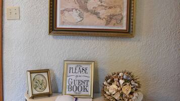 Un mapa enmarcado de Norteamérica en una pared, un letrero que dice “Por favor, firme su libro de visitas” sobre una mesa, y un arreglo floral decorativo.