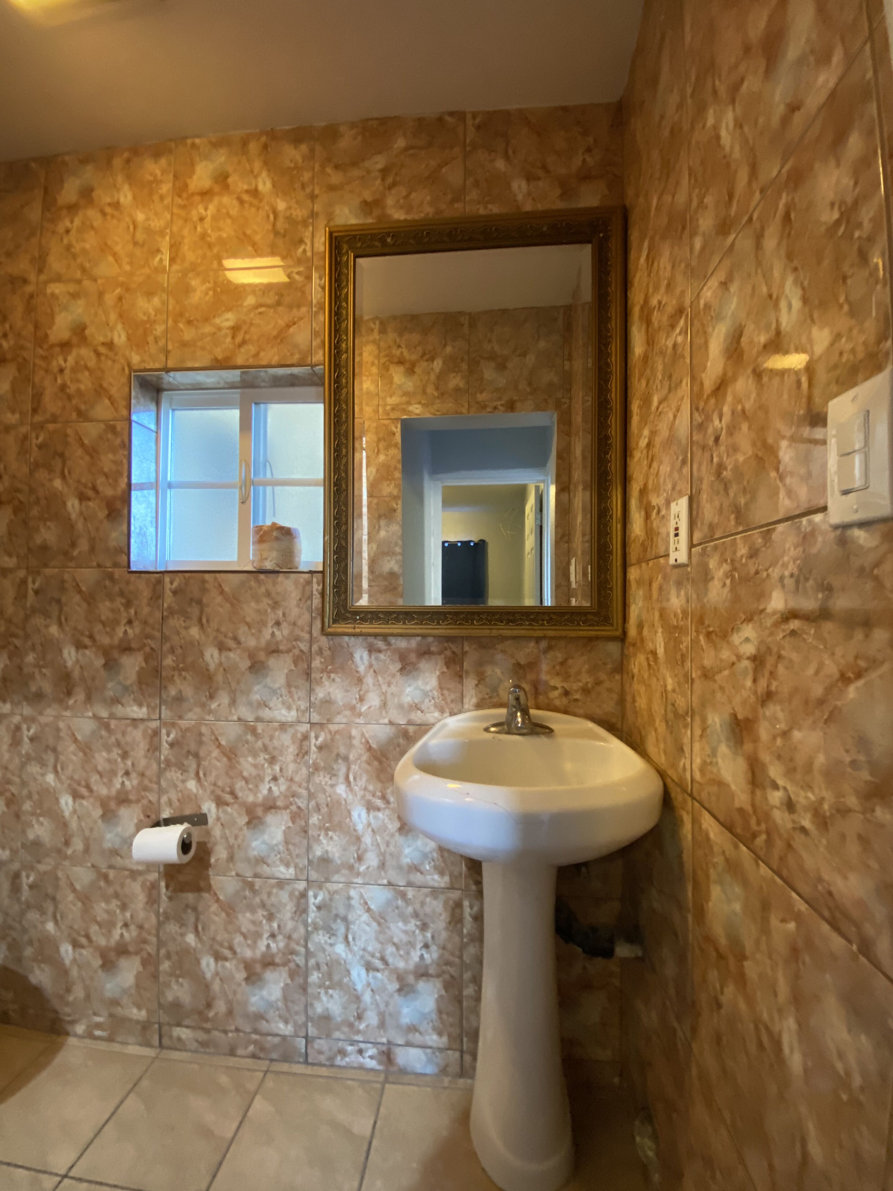 A bathroom with marble walls, a sink, a mirror, and a toilet paper holder.