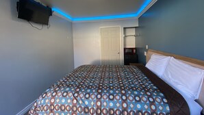 A bedroom with a bed, a TV mounted on the wall, a door, and a shelf with a microwave. - Sands Inn (South Gate)