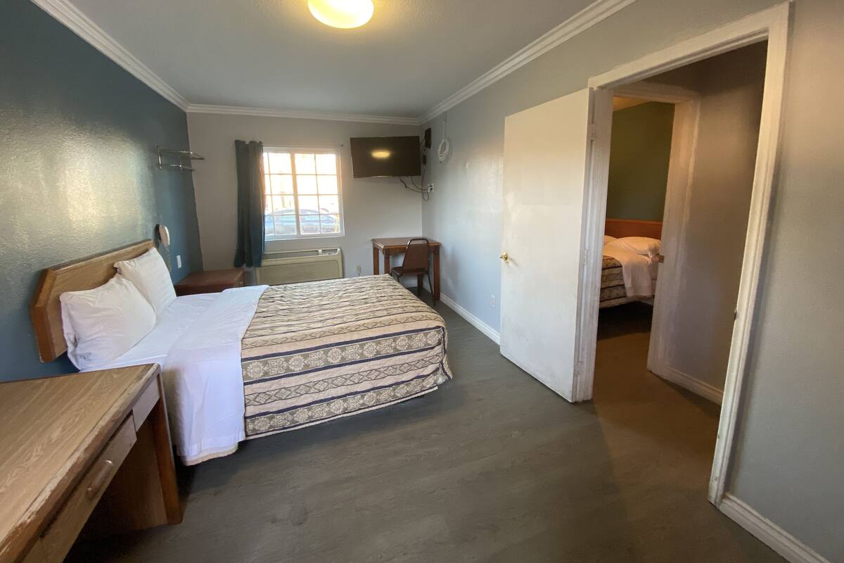 Habitación de hotel con cama, escritorio, silla, televisor montado en la pared y ventana con cortinas.