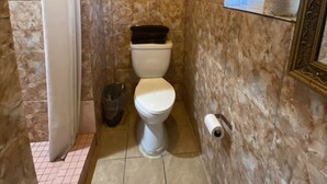 A bathroom with a toilet, a trash bin, and a toilet paper holder. - Sands Inn (South Gate)