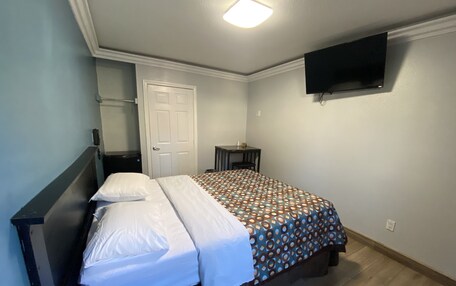 A bedroom with a bed, a bedside table, a chair, a desk, a TV mounted on the wall, and a door.