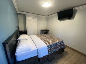 A bedroom with a bed, a bedside table, a chair, a desk, a TV mounted on the wall, and a door. - Sands Inn (South Gate)