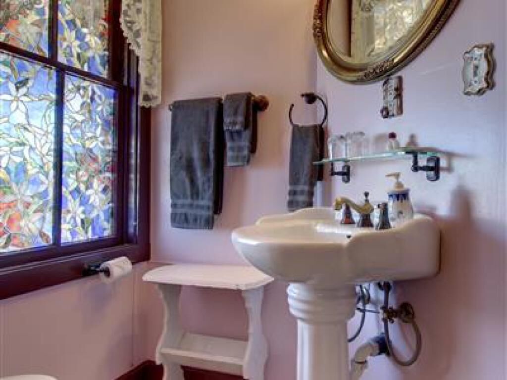 A bathroom with a white pedestal sink, a mirror above it, and a window with stained glass.