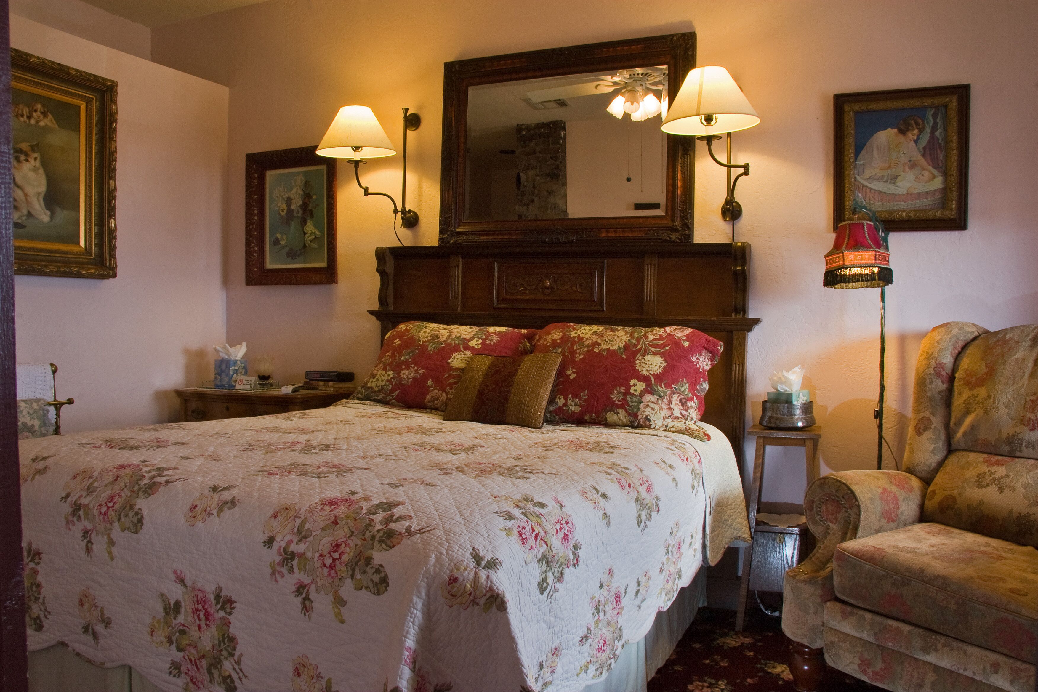 A bedroom with a large bed, two wall-mounted lamps, a wooden headboard, a chair, and a small table with a lamp.