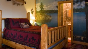 Ein gemütliches Cabin-Zimmer mit einem Bett, einem Fisch an der Wand, einem Gemälde eines Sees und einer Holztür, die zu einem Badezimmer führt.