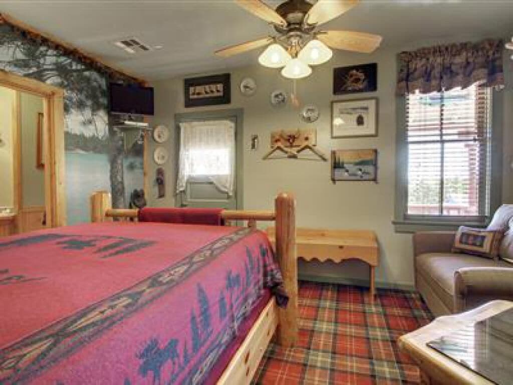 A bedroom with a bed, a wooden nightstand, a chair, a window with blinds, and a ceiling fan.