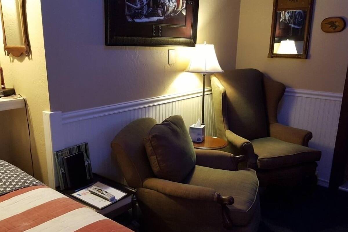 A hotel room with two armchairs, a lamp, a television, and a bed with an American flag.