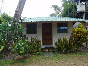 Une petite maison avec un toit vert, une porte en bois et une fenêtre.