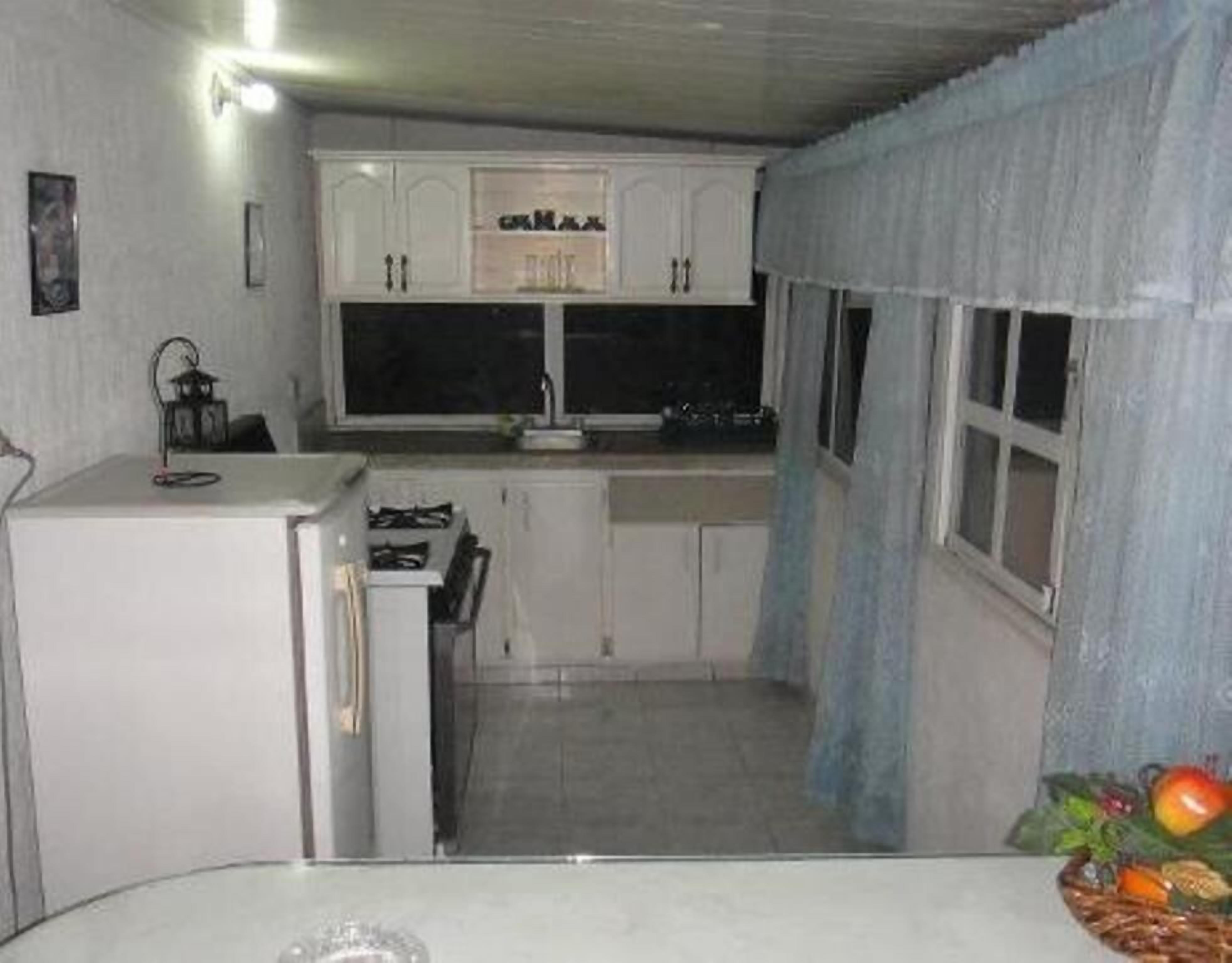 A compact kitchen with white cabinets, a small refrigerator, and a window with a curtain.