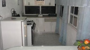 Eine kleine Küche mit weißen Schränken, einem kleinen Kühlschrank und einem Fenster mit Vorhang.