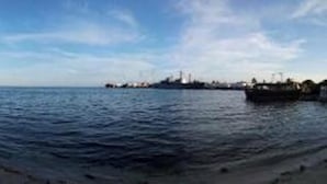 Eine Küstenlandschaft mit sandigem Strand, ruhiger See und einer entfernten Skyline.