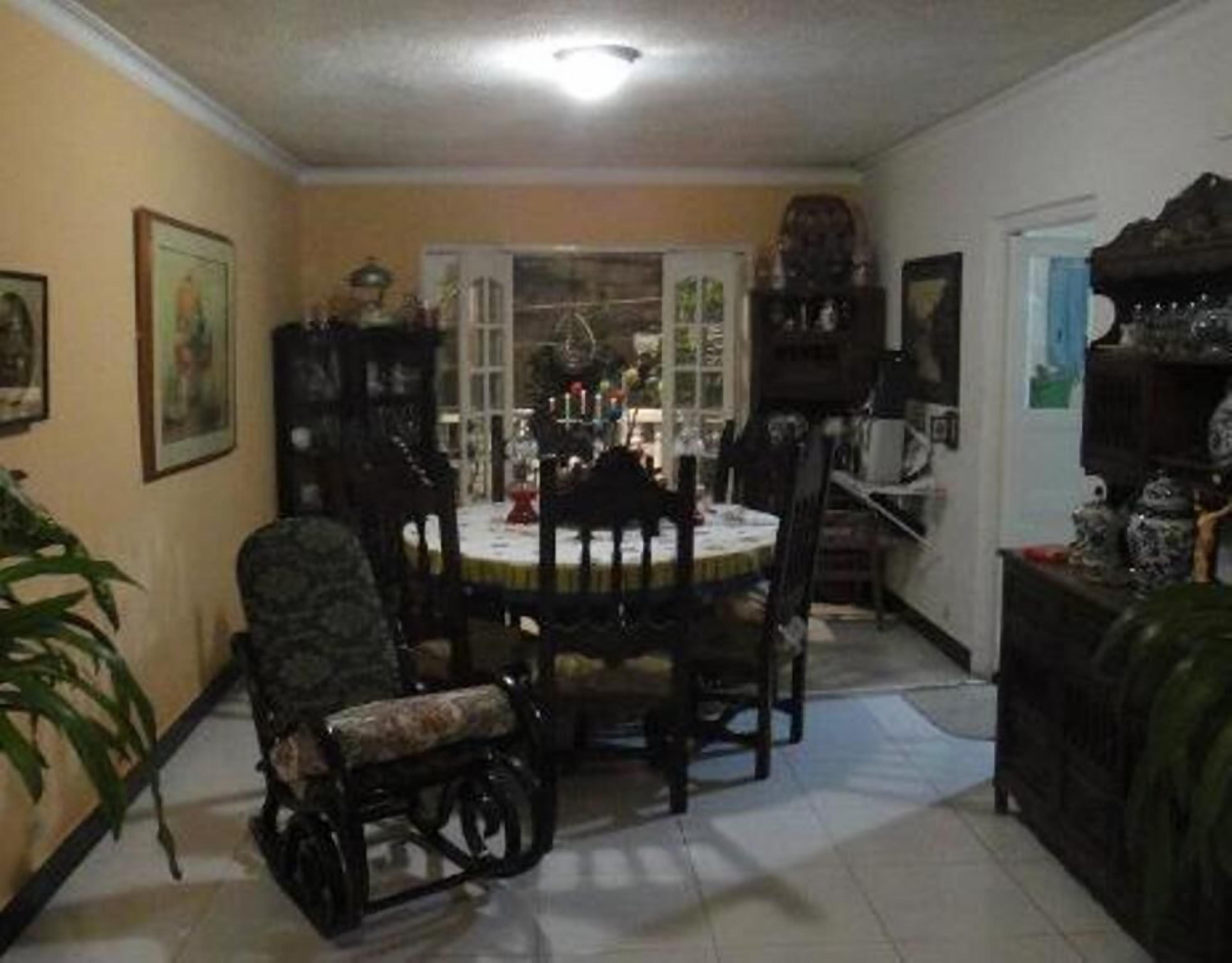 A dining area with a round table and chairs, surrounded by walls with framed pictures and a dark wooden cabinet.