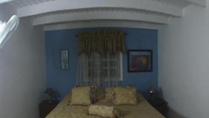 Ein Schlafzimmer mit einem Bett, zwei Nachttischen, einem Fenster mit Vorhängen und einem Gemälde an der Wand.