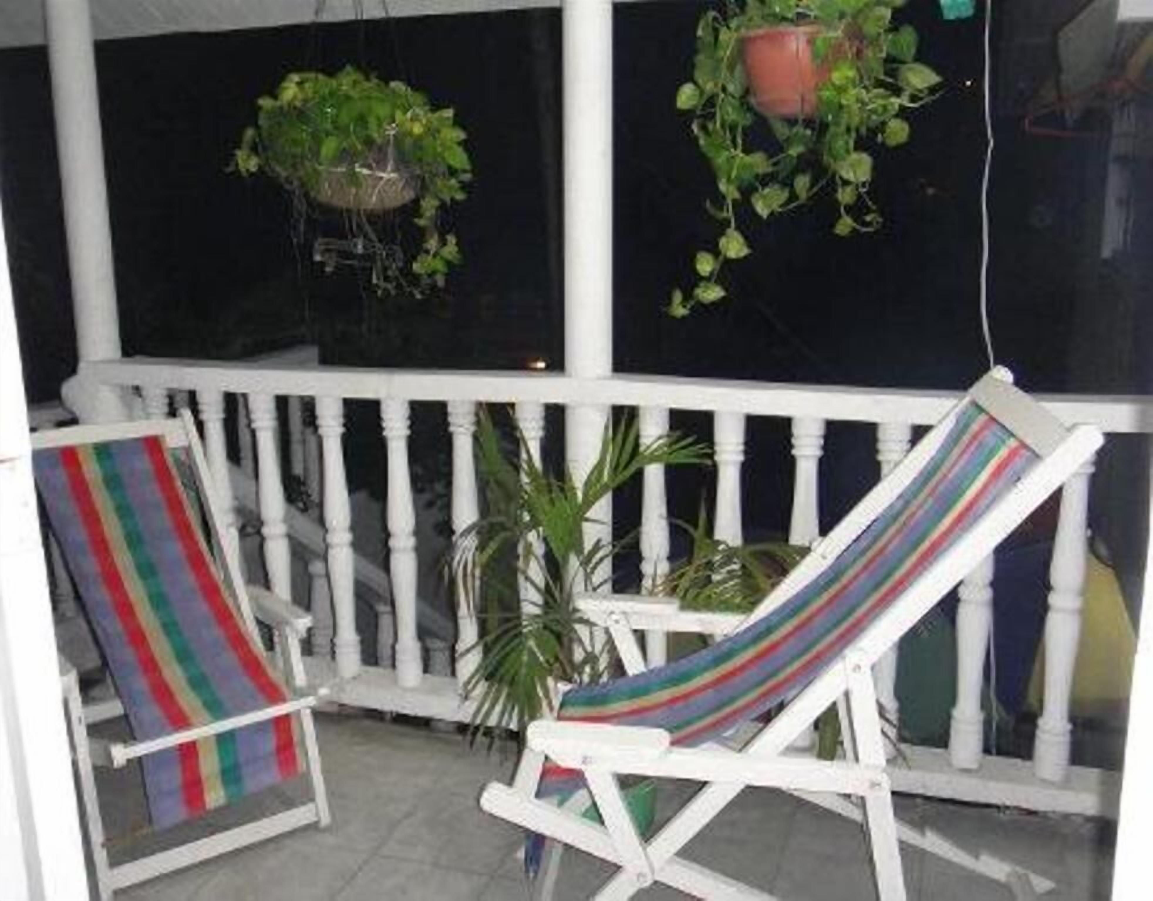 Un porche blanco con dos sillones de lounge, uno con una toalla a rayas. Hay dos macetas colgantes con plantas verdes.