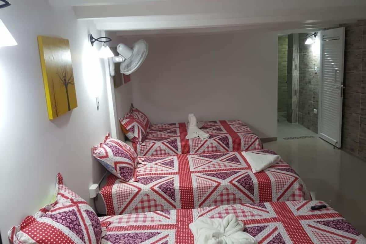 A room with a bed covered in red and white checkered bedding, a standing fan, and a yellow wall art piece.