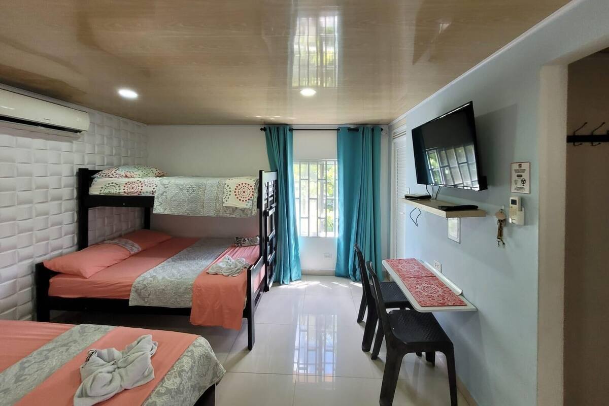 A dormitory room with bunk beds, a desk, a chair, a TV, and an air conditioning unit.
