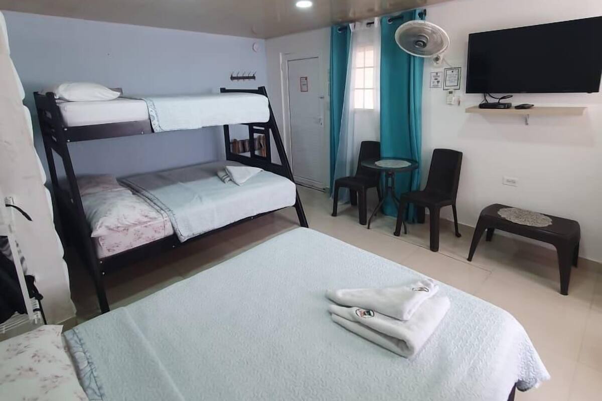 A room with a bunk bed, a desk, a chair, a TV, and a fan.