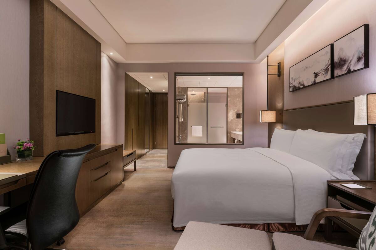 A hotel room with a bed, a desk with a chair, a television, and artwork on the wall.