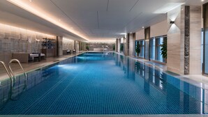 A modern indoor swimming pool with clear blue tiles, a long poolside area with seating, and a view of the sky through large windows. - DoubleTree by Hilton Hotel Shiyan (Shiyan)