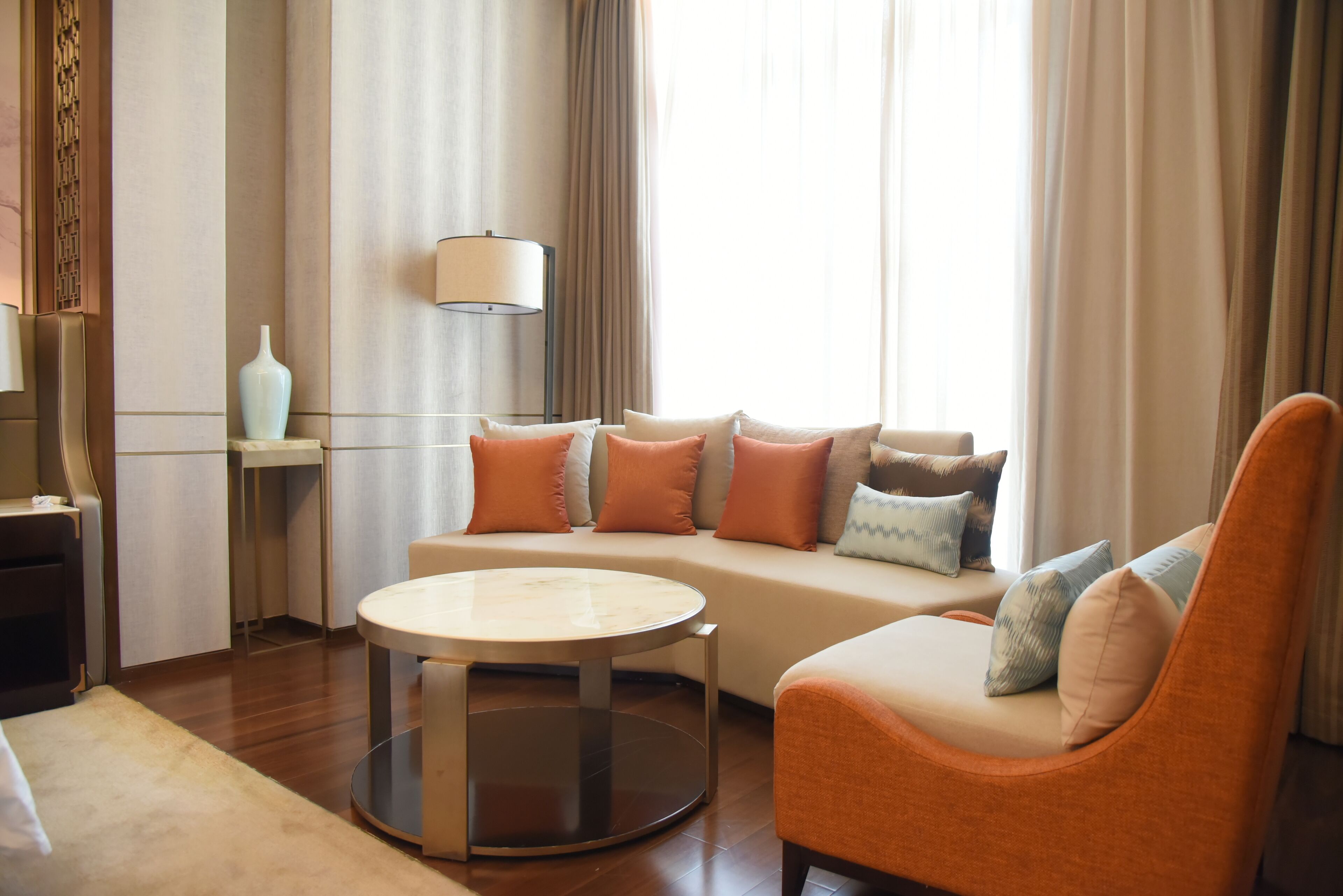 Un salon moderne avec un canapé, une table basse ronde et un fauteuil. On y trouve une lampe sur un pied et un vase sur une étagère.