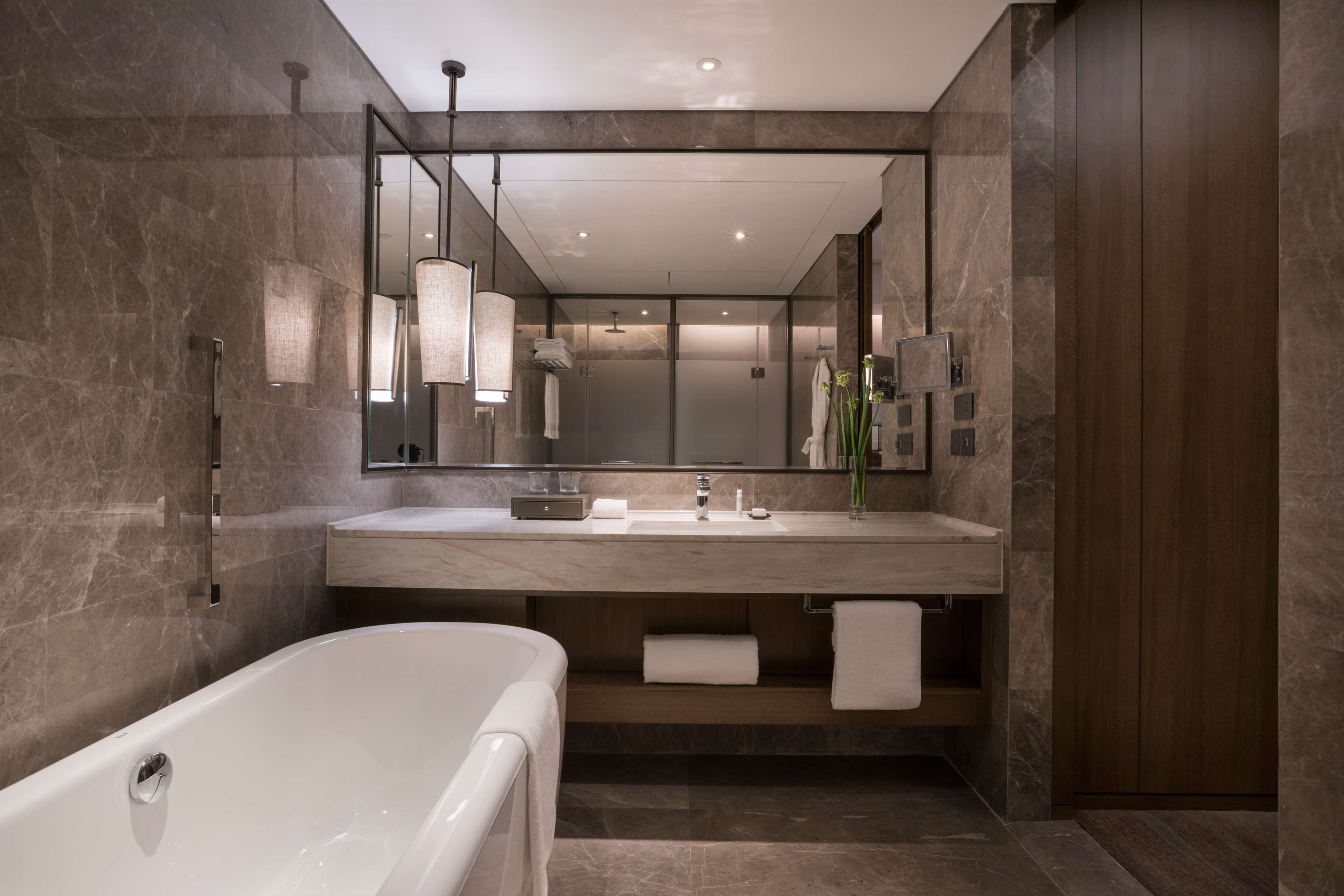 A modern bathroom with a large mirror, a bathtub, and a vanity with a sink and towel rack.