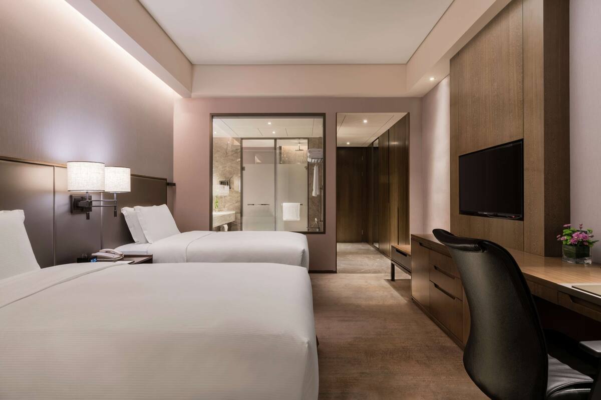 A hotel room with two beds, a desk with a chair, a TV, and a mirror.