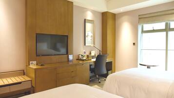 A hotel room with two beds, a desk, a TV, and a window.