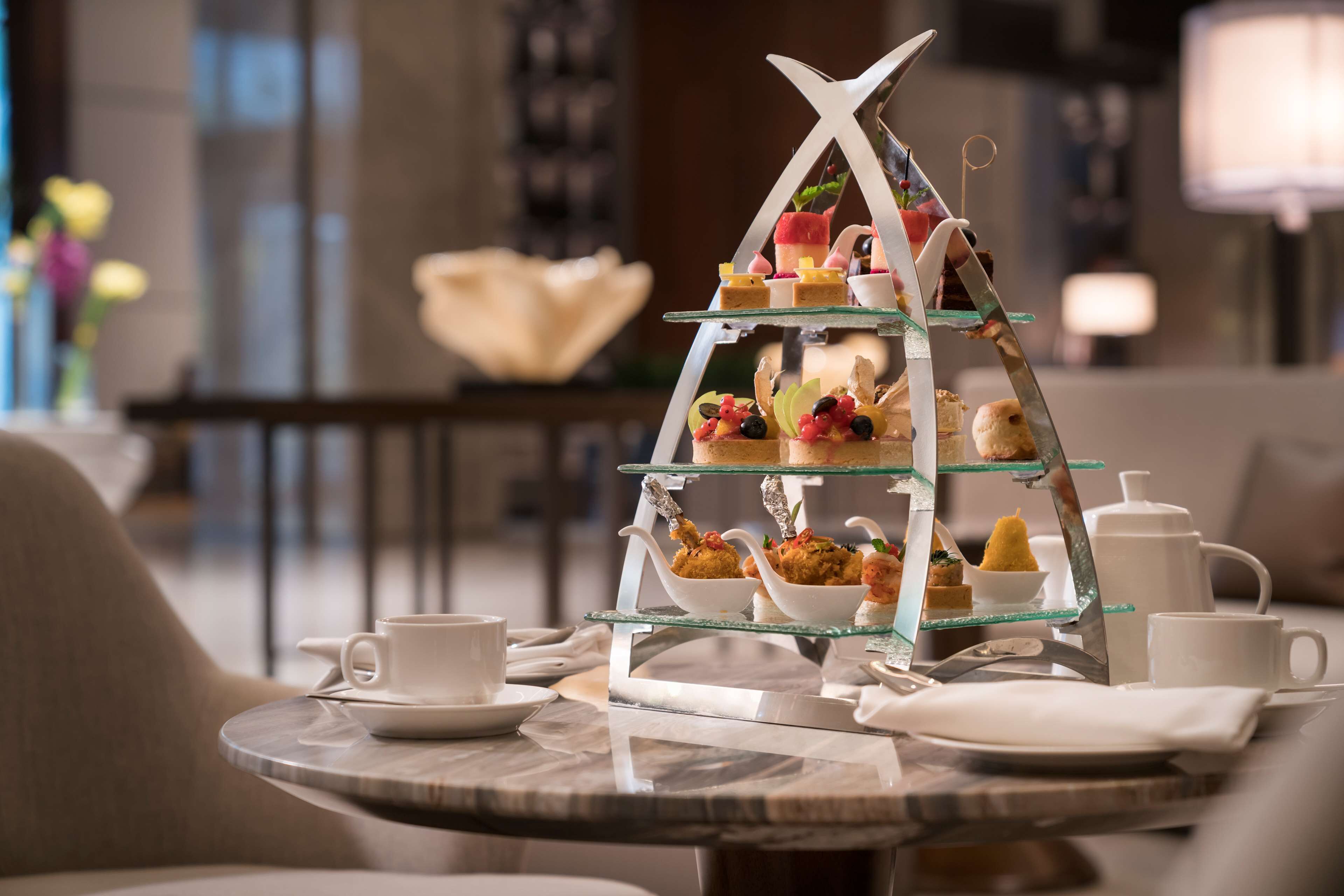 A tiered dessert display on a table with white cups and saucers, in a modern interior with a neutral color palette.