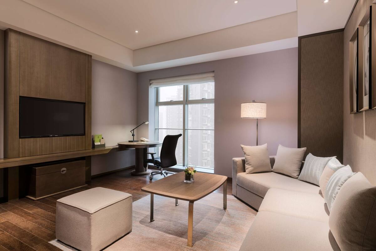 A modern living room with a flat-screen TV, a desk, a sofa, and a lamp.